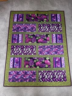 a quilted purple and green table runner with flowers in the center, on carpet