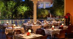 an outdoor dining area with tables, chairs and candles lit up at night near the water