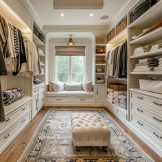 a large walk in closet with lots of drawers and white furniture, including a bench