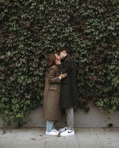 a man and woman kissing in front of a green wall