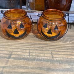 two pumpkin shaped glass jars sitting on top of a wooden table