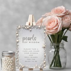 there is a sign with pearls on it next to some pink roses and a jar