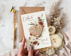 a person holding up a card with a heart on it next to flowers and a pen