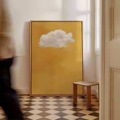 a large yellow painting with a white cloud on it in a room next to a small stool