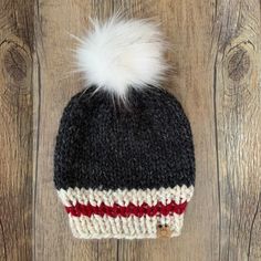 a black, white and red knitted hat with a fur pom