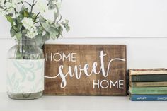 a wooden sign that says home sweet home next to some books and a vase with flowers