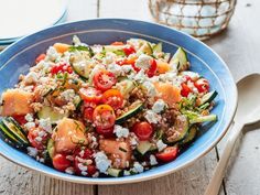 a blue bowl filled with cucumber, tomato and feta cheese salad on top of a wooden table