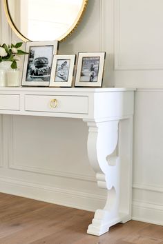 a white console table with three pictures and a vase on it in front of a mirror