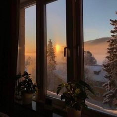 the sun is setting in front of some snow covered trees and mountains as seen from an open window