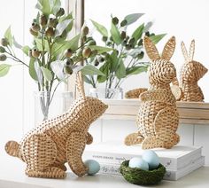 two wicker rabbits sitting on top of a table next to some eggs and plants