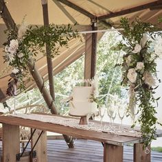 a table topped with a white cake covered in flowers and greenery under a tent