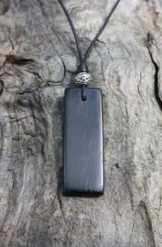 a black pendant is sitting on a piece of tree bark with a silver bead around it