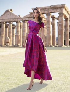 a woman standing in front of an ancient building wearing a purple dress and high heels