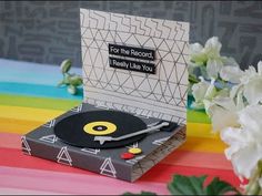 a record player sitting on top of a table next to flowers and a rainbow colored background