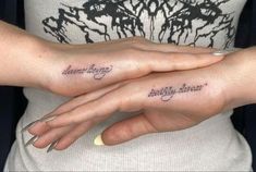 two women with matching tattoos on their hands, both holding each other's fingers