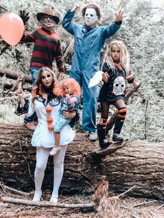 three children dressed up in halloween costumes standing on a fallen tree with their hands raised