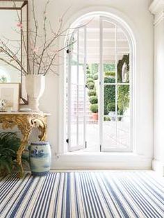 a room with an arched glass door and blue and white striped rug on the floor