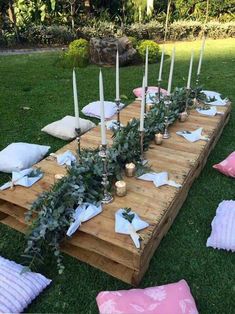 a wooden table with candles and greenery on it in the middle of some grass