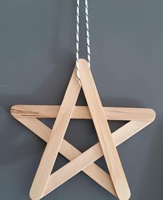 a wooden star ornament hanging from a string on a gray wall with two white ropes