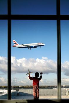 a little boy standing in front of a window looking out at an airplane taking off