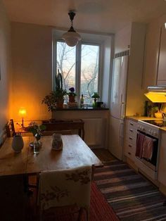 a kitchen with a table, stove and sink in it next to a window filled with potted plants