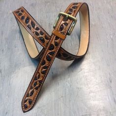 a leather belt with an intricate design on the front and side, sitting on a metal surface