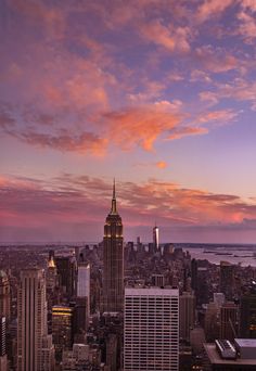 the city skyline is lit up at night with pink clouds and blue sky in the background