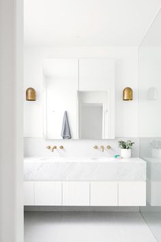 a white bathroom with two sinks and gold faucets