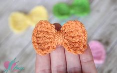 a hand holding an orange crocheted bow brooch