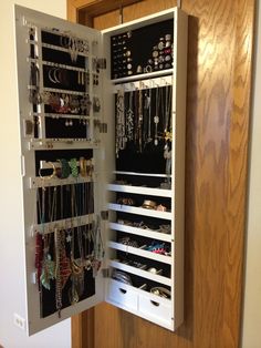 an open jewelry cabinet with lots of necklaces and bracelets hanging on the doors