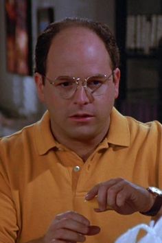 a man wearing glasses is looking at something in his hand as he eats food from a plate