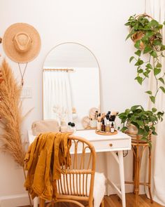 a white desk topped with a mirror next to a chair and table covered in plants