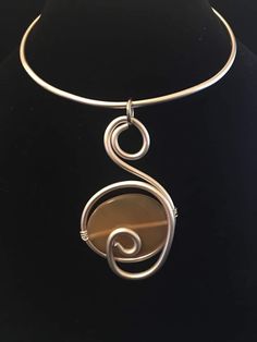 a silver necklace with a spiral design hanging from it's side on a black background