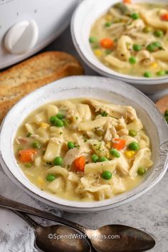 two bowls filled with chicken noodle soup on top of a table next to bread