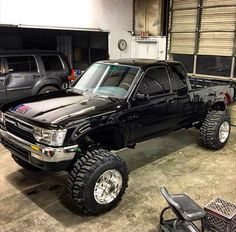 a black truck parked in a garage next to two other trucks with tires on them