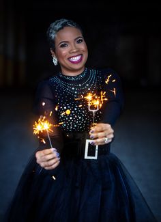 a woman holding sparklers in her hands and smiling at the camera while wearing a black dress