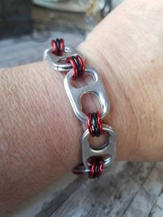 a close up of a person's arm wearing a metal bracelet with red and black beads