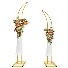 two tall gold stands with flowers and greenery on them, one holding a bouquet