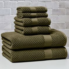 stack of folded towels in front of a brick wall with white bricks on it and one folded green towel