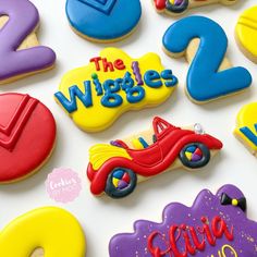 decorated cookies with numbers and cars are displayed on a white table top, including one for the wiggles