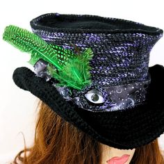 "This Fae eye top hat adds a funky celestial witchy magic feel to your renfair costume, a festival, a concert, or just for fun! I've crocheted this with a firm stitch in a deep kettle dyed purple merino against black, giving subtle flecks of night sky color throughout the hat. I've topped it off with a satin ribbon band printed with moons against the night sky, and green feathers. I detailed the eye as part of the hat band, with faux leather lids, and a crocheted edging. I've also wired the brim Mystical Halloween Festival Costume Hats And Headpieces, Fantasy High Crown Hat For Costume Party, Fantasy High Crown Costume Hat, Adjustable Fantasy Hats For Themed Events, Mystical Halloween Costume Hats And Headpieces, Fantasy Themed Adjustable Hats, Whimsical Adjustable Top Hat For Festivals, Witchy Adjustable Mini Hats For Festivals, Adjustable Witchy Mini Hats For Festivals