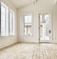 an empty room with white walls and wooden floors, two windows on either side of the door