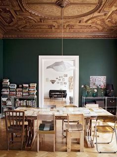 a dining room with green walls and wooden floors, an ornate ceiling is decorated with bookshelves