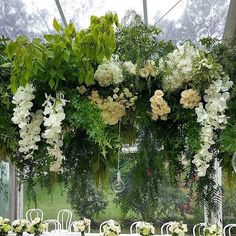 an arrangement of white flowers and greenery decorates the top of a tented table