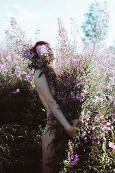 a woman standing in the middle of a field with purple flowers on her chest and eyes closed