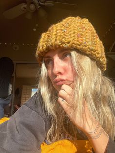 a woman with blonde hair wearing a yellow knitted hat and looking at the camera