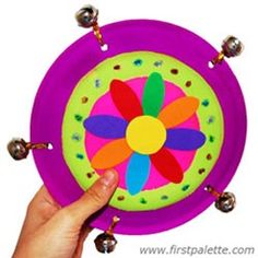 a hand holding up a colorful paper plate with bells on the sides and a flower design on it