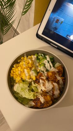 a bowl of salad next to an open laptop computer