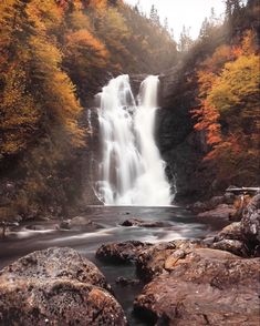 a waterfall surrounded by rocks and trees in the fall time with leaves turning to orange