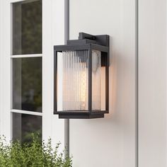 an outdoor wall light on the side of a house with potted plants next to it